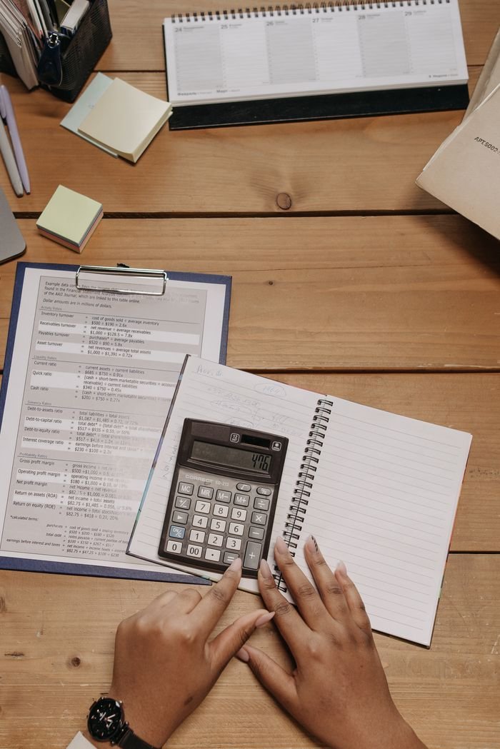 About Top view of hands using calculator on office desk surrounded by documents and sticky notes.